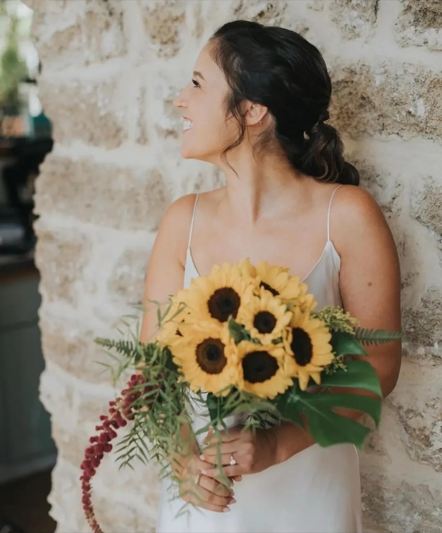 Bride holding sunflowers beside a stone wall